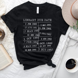 May include: Black t-shirt with white text that reads "LIBRARY DUE DATE" and lists dates from June 1980 to November 1982.