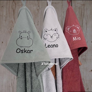 Könnte beinhalten: Drei Kapuzenhandtücher mit gestickten Tiermotiven und Namen. Die Handtücher sind grün, grau und rot. Die Tiere sind ein Nilpferd , ein Fuchs und ein Koala. Die Namen sind Oskar, Leano und Mia.