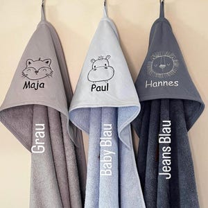May include: Three hooded towels in gray, light blue, and dark blue with embroidered animal designs and names. The towels are labeled "Grau", "Baby Blau", and "Jeans Blau".