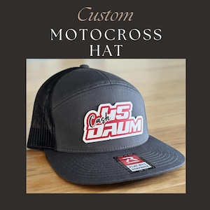 May include: Gray and black custom motocross hat with a red and white patch that says "Cash 15 Daum".
