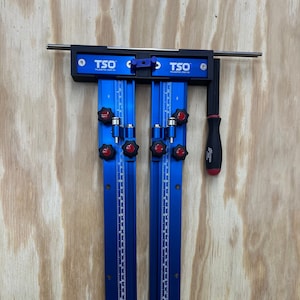 May include: A blue metal tool holder with two slots for TSO tools. The holder has a black top with the text "TSO The Adapter Drop-On" printed on it. The holder is on a wood surface. "HOLDER ONLY TSO TOOLS NOT INCLUDED" is printed in red and blue text on a white background.