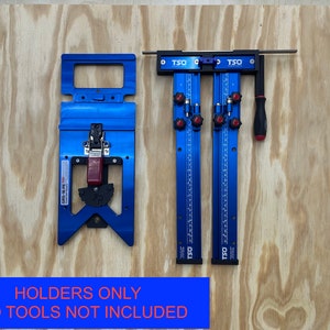 May include: Two blue and black woodworking jigs with red knobs and a red lever. The jigs are on a wood surface. The text "HOLDERS ONLY TSO TOOLS NOT INCLUDED" is printed on a blue banner below the jigs.