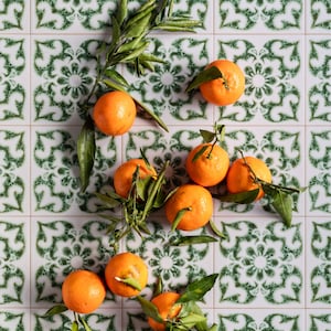 Pode incluir: Um grupo de laranjas com folhas verdes em um piso de azulejos brancos com um padrão verde e branco.