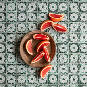 May include: A brown ceramic bowl filled with slices of pink grapefruit on a green and white tiled surface.