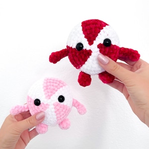 May include: Two crocheted plush toys shaped like candy. The larger toy is red and white, and the smaller toy is pink and white.