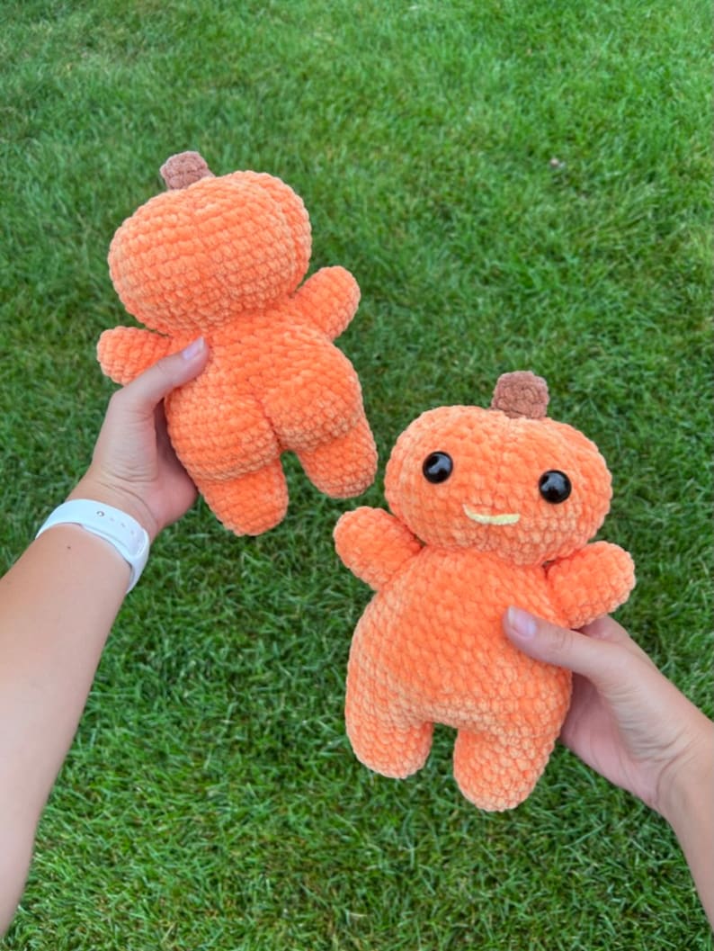 Peut inclure: Deux peluches en forme de citrouille orange au crochet avec des yeux noirs et un sourire jaune. Les citrouilles sont tenues dans les mains de deux personnes.