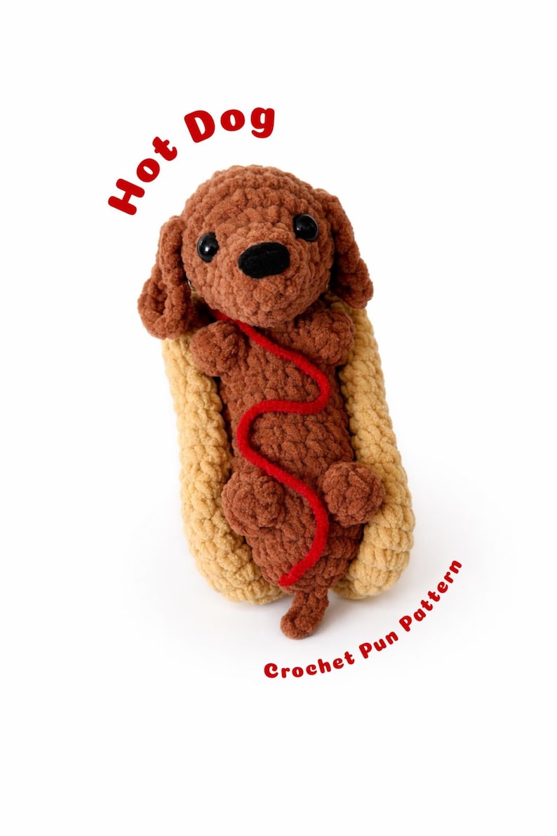 Op de afbeelding: Een handgemaakte gehaakte hotdog met een bruine hond in een bruin broodje, met een rood touwtje. De woorden "Hot Dog" en "Crochet Pun Pattern" zijn in het rood geschreven.