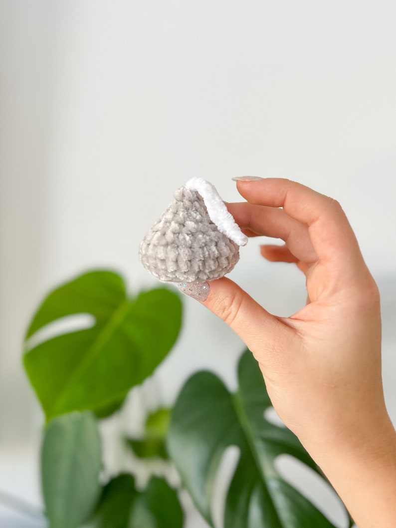 May include: A small gray and white crocheted ornament shaped like a teardrop. The ornament has a white crocheted loop at the top.