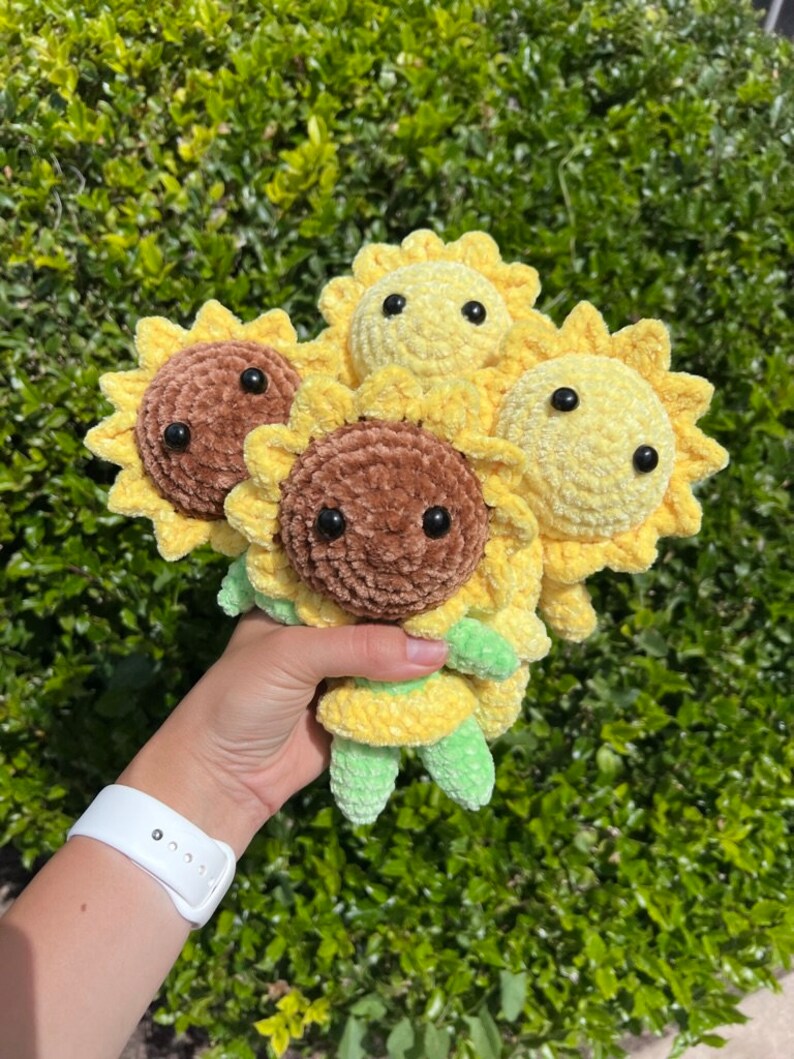 May include: Four crocheted sunflower plush toys. Two are brown and two are yellow. The sunflowers have black eyes and green stems.