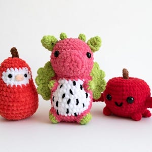 May include: Three handmade crochet toys: a red pear-shaped owl, a pink dragon fruit, and a red apple with a smiling face. The toys are made of soft yarn and are suitable for children.