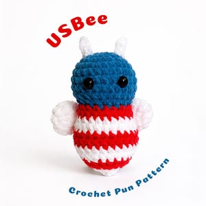 May include: A crocheted bee plush toy featuring a blue head with black eyes and white antennae, and a body with horizontal red and white stripes. The text USBee is printed in red above the toy, and Crochet Pun Pattern in blue below it.