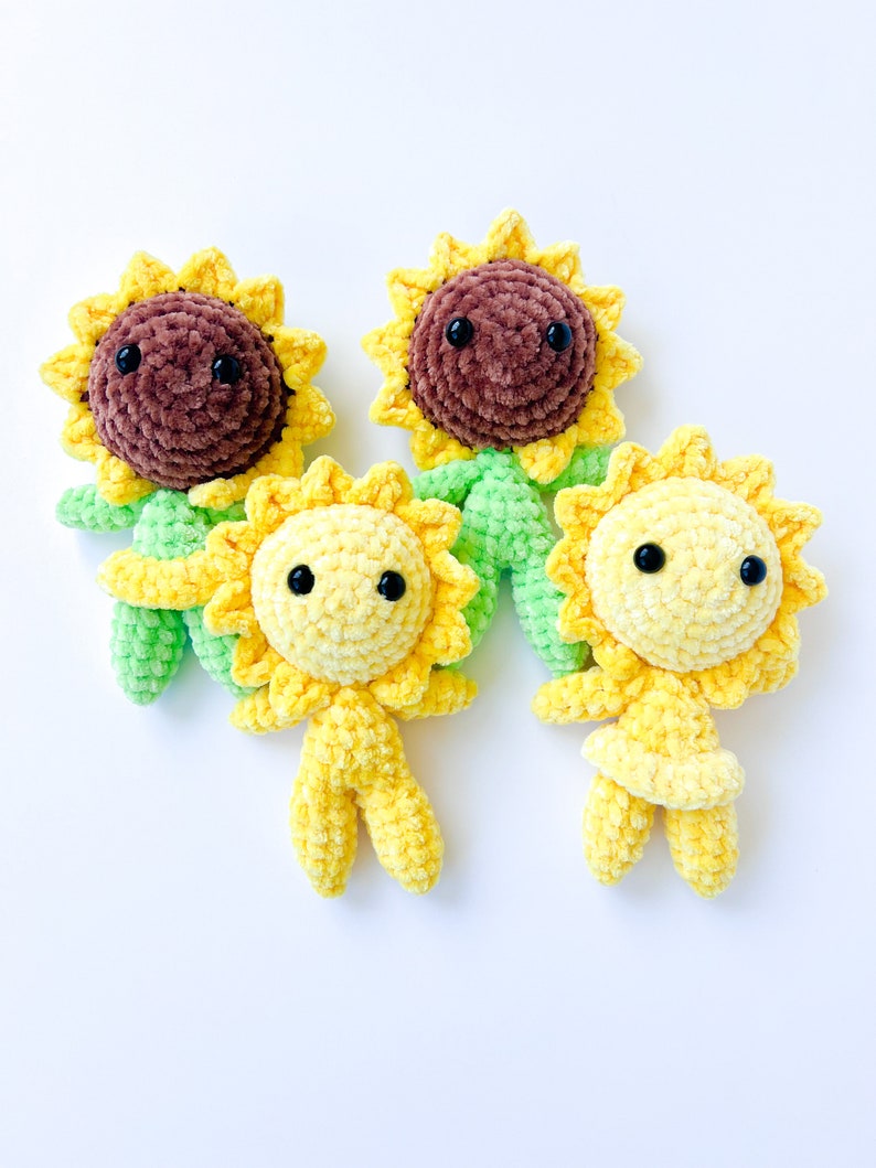 May include: Three crocheted sunflower plush toys. One sunflower is brown with green leaves, and the other two sunflowers are yellow with green leaves. All three sunflowers have black eyes.