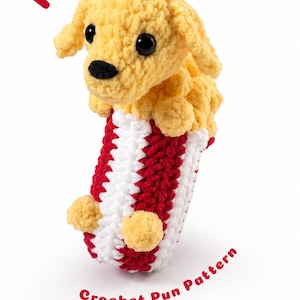 May include: A yellow crocheted puppy plush emerging from a red and white striped popcorn bucket. The text Pupcorn is printed in red above the puppy, and the text Crochet Pun Pattern is printed in red below the bucket on a white background.