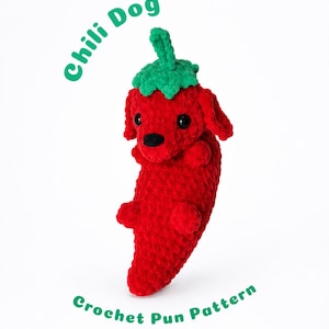 May include: A red crocheted plush toy shaped like a chilli pepper with a dog head, black eyes, and a green stem on top. The text "Chili Dog" appears in green above the toy, and "Crochet Pun Pattern" is written in green below the plush figure.