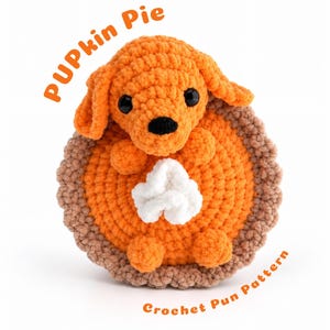 May include: A crocheted stuffed animal shaped like a puppy sitting in a pumpkin pie. The puppy is orange with black eyes and a black nose. The pie has an orange filling, a brown crust, and a white dollop of whipped cream. Text reads PUPkin Pie.
