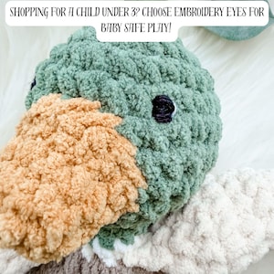May include: A handmade plush duck toy with a green head, tan beak, and white and gray wings. The text "SHOPPING FOR A CHILD UNDER 3? CHOOSE EMBROIDERY EYES FOR BABY SAFE PLAY!" is displayed above the toy.