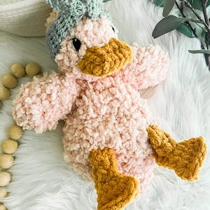 May include: A pink crocheted duck plush toy with a green bow on its head and yellow crocheted feet.