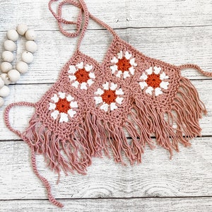 May include: A pink crochet top with white and orange flowers and fringe trim.