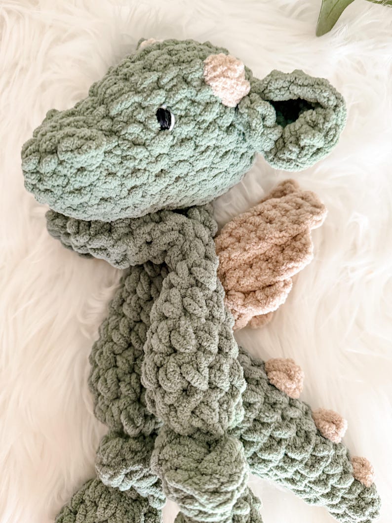 Peut inclure: Un dragon en crochet fait &agrave; la main, dans des tons de vert et de beige. Le jouet en peluche pr&eacute;sente un design d&eacute;taill&eacute; avec des &eacute;cailles textur&eacute;es, de petites cornes beiges et des ailes. Le dragon a une expression amicale avec un &oelig;il noir.