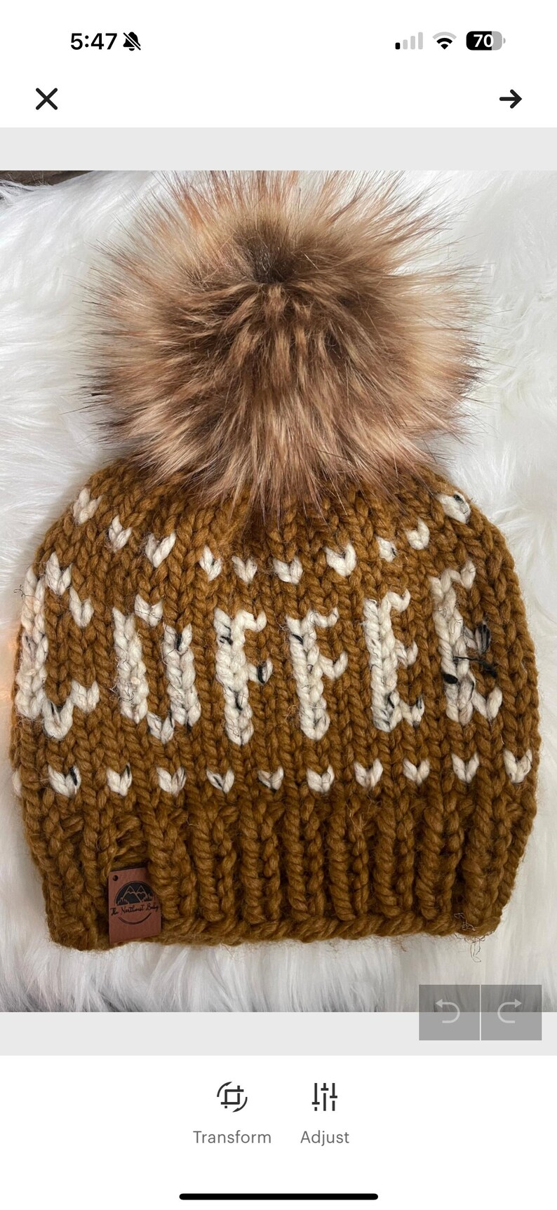 May include: A brown knit hat with the word "COFFEE" in white block letters. The hat features a large, fluffy, brown pom-pom on top. A small, brown tag is sewn on the brim.