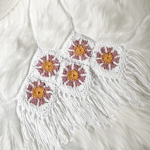 May include: White crochet top with pink and yellow flower details and fringe trim.