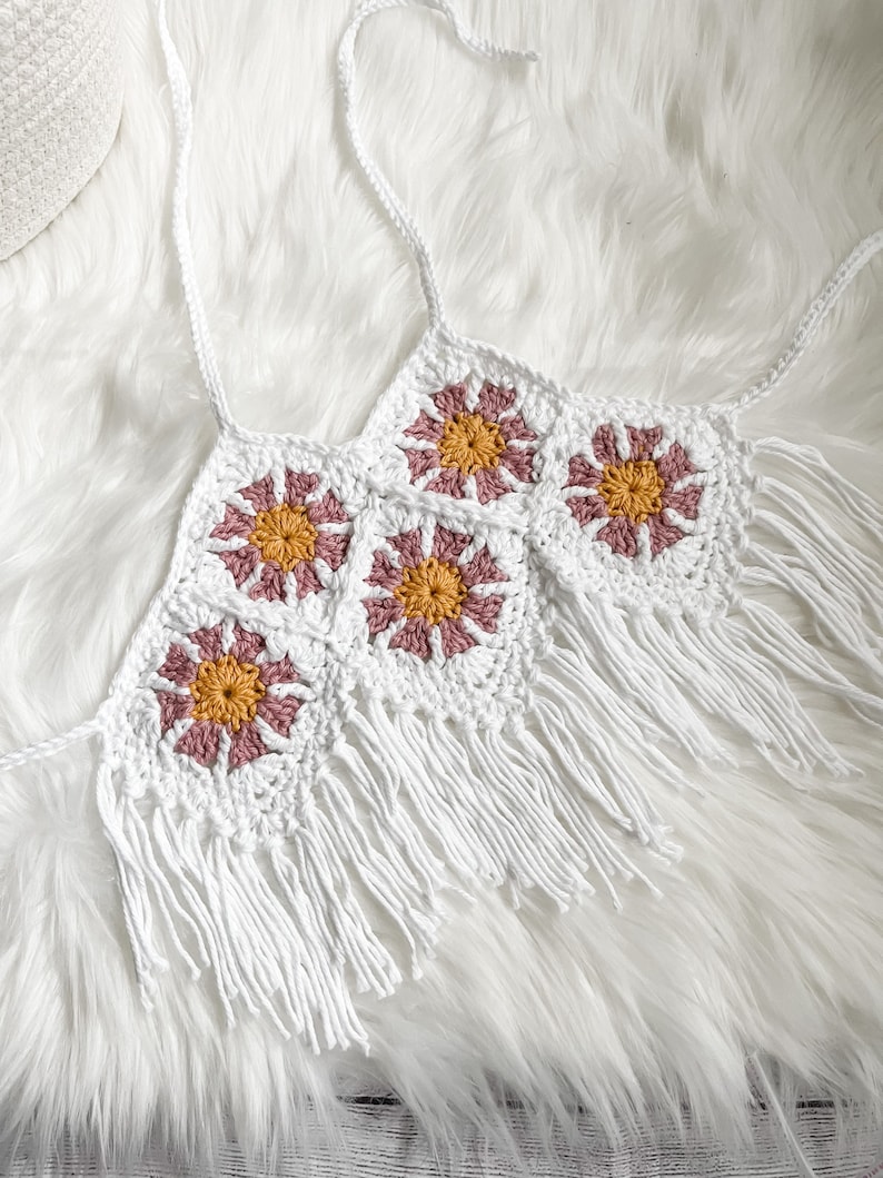 May include: White crochet top with pink and yellow flower details and fringe trim.