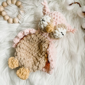 May include: A crocheted owl toy with pink, brown, and yellow yarn. The owl is lying on its back with its eyes closed.