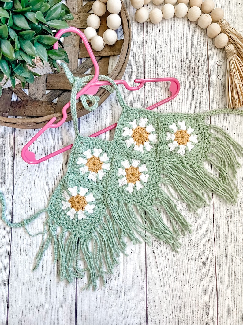 May include: A green crochet halter top with white and yellow daisy flowers and fringe trim.