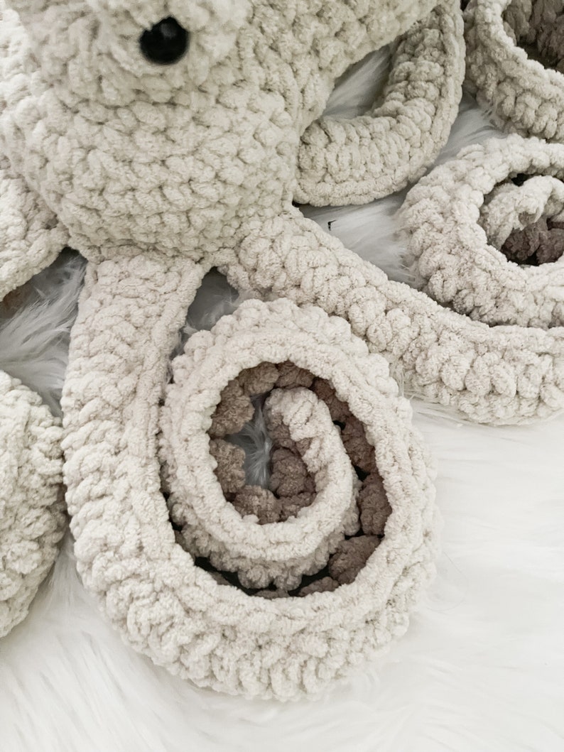 Pode incluir: Um brinquedo de polvo de croch&ecirc; em branco e marrom. O polvo tem oito tent&aacute;culos, que est&atilde;o enrolados em forma de espiral.