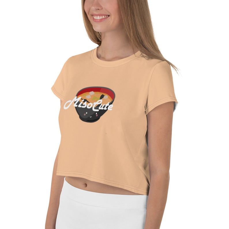 May include: A peach colored cropped t-shirt with short sleeves featuring a cartoon illustration of a bowl of miso soup with the text "MisoCute" in white.