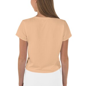 May include: A peach-colored cropped t-shirt with short sleeves. The shirt is made of a soft, comfortable fabric and has a relaxed fit.
