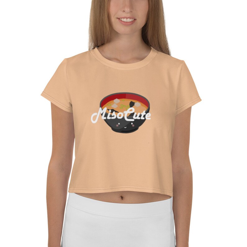 May include: A peach colored cropped t-shirt with short sleeves featuring a cartoon illustration of a bowl of miso soup with the text "MisoCute" in white.