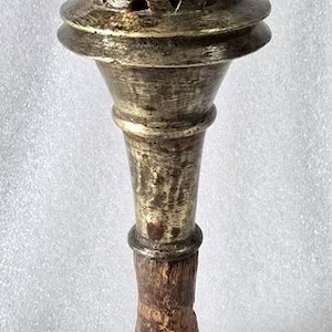 May include: An antique brass incense burner with a conical lid featuring triangular cutouts. The burner has a bulbous top, a long, slender stem, and a wooden base. The metal has a tarnished, aged appearance.