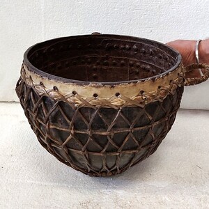 May include: A large, round, brown woven basket with two handles. The basket is made of dark brown leather and has a woven pattern. The basket is sitting on a white surface.