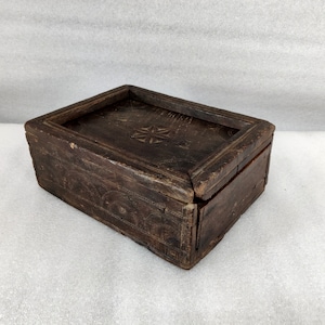 Puede incluir: Una caja de madera marrón oscuro con un diseño tallado en la tapa. La caja tiene una tapa con bisagras y un diseño sencillo.