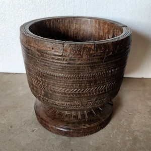 Könnte beinhalten: Eine dunkelbraune Holzschale mit einem geschnitzten Design. Die Schale hat einen breiten Boden und eine abgerundete Oberseite. Es ist ein traditioneller Schalen-Stil.