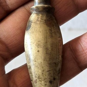 May include: A vintage brass bottle stopper with a unique shape. The stopper has a rounded body and a handle with the word "INDIA" engraved on it. The brass has a warm, aged patina.