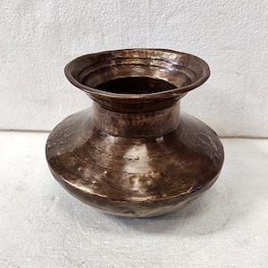 May include: A hammered copper vase with a wide, rounded base and a flared, slightly scalloped rim. The vase has a rustic, antique look and is a beautiful decorative piece.