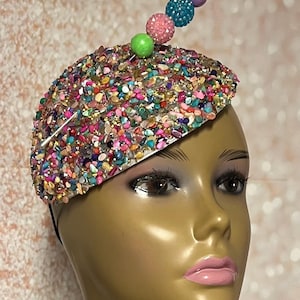 May include: A white hat with a colorful, sparkly design. The hat has a small pin with a row of colorful beads on top.