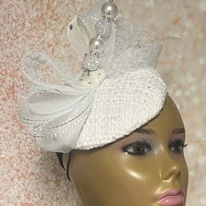 May include: White hat with a white and silver feather and pearl embellishments.