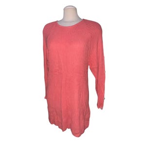 May include: Coral-colored long-sleeve sweater dress. The dress features a ribbed knit texture and a round neckline. The sleeves are long with a button detail at the cuffs. The dress is displayed on a mannequin.