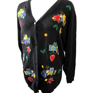 K&ouml;nnte beinhalten: Schwarzer Cardigan-Pullover mit Weihnachtsmotiv. Der Pullover zeigt bunte gestickte Engel, Sterne und Stechpalmenbl&auml;tter.
