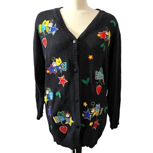K&ouml;nnte beinhalten: Schwarzer Cardigan mit V-Ausschnitt und Knopfleiste. Der Pullover ist mit bunten gestickten Sternen, Engeln und anderen weihnachtlichen Motiven verziert.