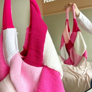 Könnte beinhalten: Eine rosafarbene und weiße gestrickte Einkaufstasche mit Patchwork-Muster. Die Tasche hängt an einem Haken und spiegelt sich in einem Spiegel mit dem Text "Feeling Good" darüber.