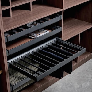 May include: A dark wood closet organizer featuring multiple shelves, a pull-out tray with a woven basket, a flat storage drawer, and a retractable metal rack designed for hanging trousers or garments, all integrated into a modular storage system.