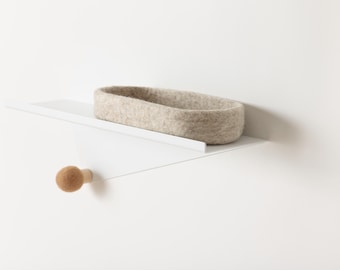 May include: A white shelf with a light brown felt basket and a wooden knob. The shelf is angled and mounted to a white wall.