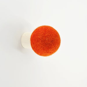 May include: A small, orange felt ball attached to a white wooden base. This is a wall-mounted hook.
