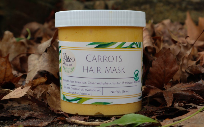 May include: A jar of "Carrots Hair Mask" with a white lid and a label featuring green leaf accents. The jar contains a yellow-orange product and is set against a backdrop of fallen leaves. The label lists ingredients.