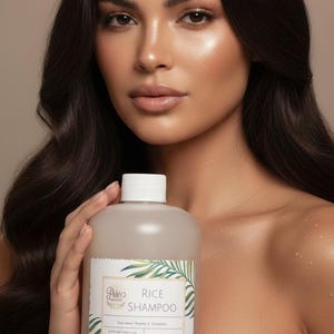 Puede incluir: Una botella de champ&uacute; de arroz se sostiene frente a una mujer. La botella es de color beige claro con una tapa blanca y una etiqueta con ilustraciones de hojas verdes y el texto "Rice Shampoo". La mujer tiene el pelo largo y oscuro y lleva una camiseta blanca.