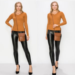 Puede incluir: Una mujer lleva un su&eacute;ter de punto marr&oacute;n y leggings de cuero negro. Lleva un bolso de cuero marr&oacute;n cruzado con cierre de solapa.